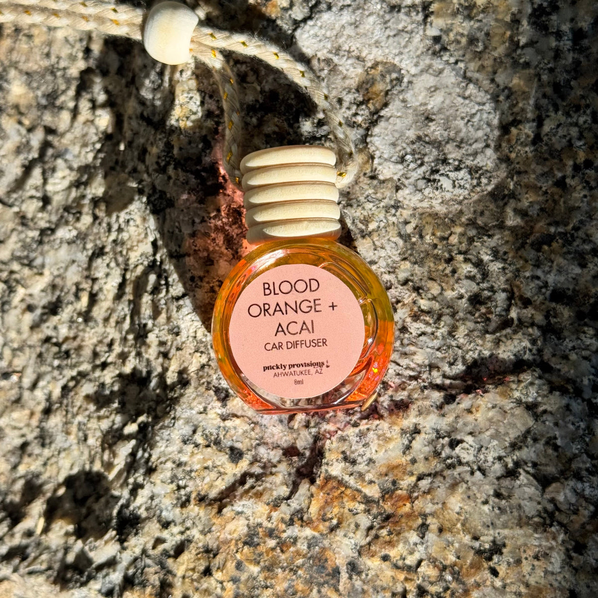 Blood Orange + Acai car diffuser hanging on a textured stone wall