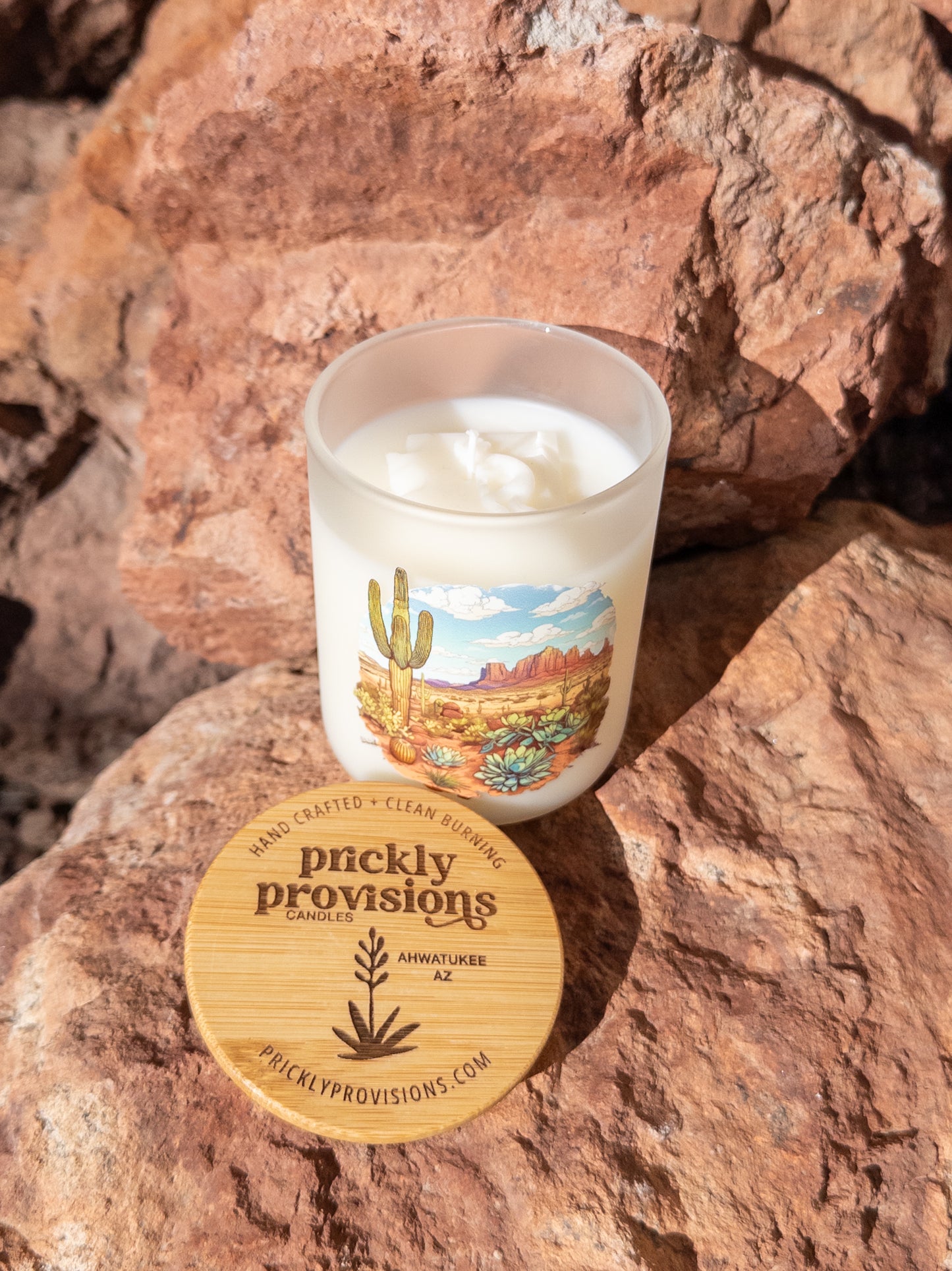 Candle with a desert-themed label on a rock, featuring the brand 'Prickly Provisions'.