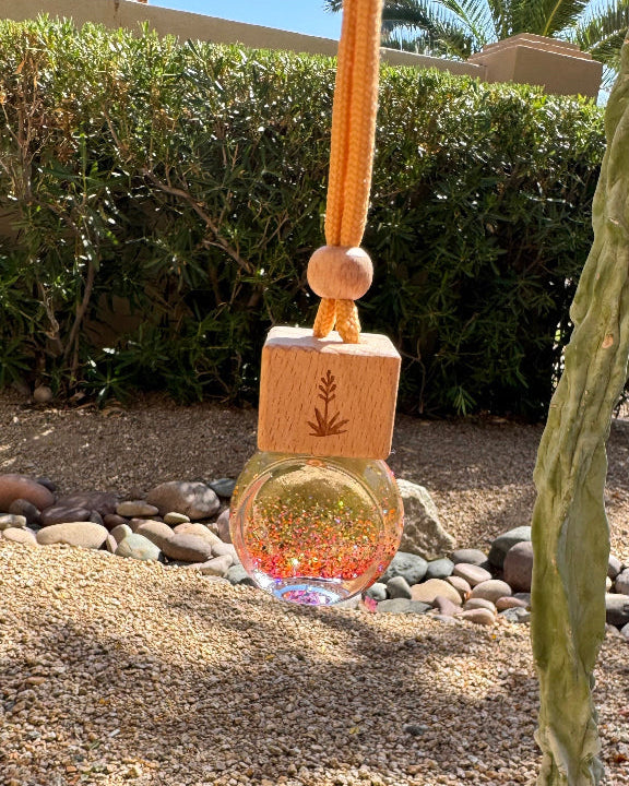 Desert Sun 8 mL hanging car diffuser with gold and iridescent glitter, engraved wooden lid, and orange cord.