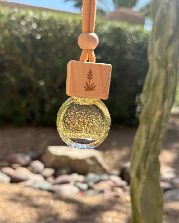 Mango + Coconut Milk 8 mL hanging car diffuser with amber-toned glass, gold glitter, engraved wooden lid, and orange cord.