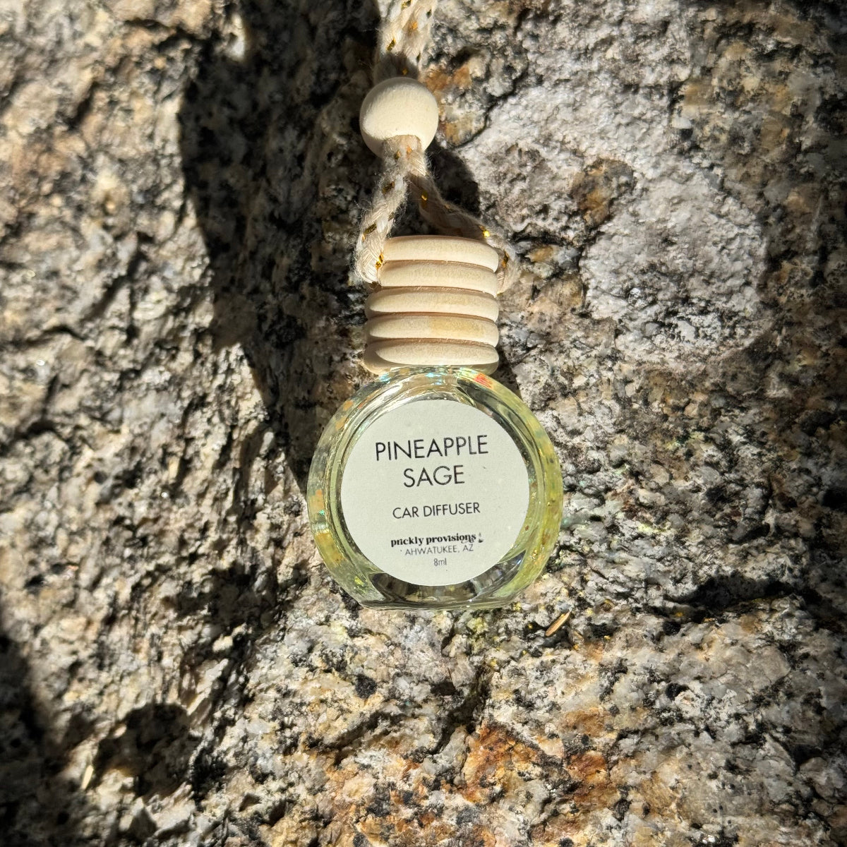 Pineapple Sage car diffuser hanging on a textured stone wall