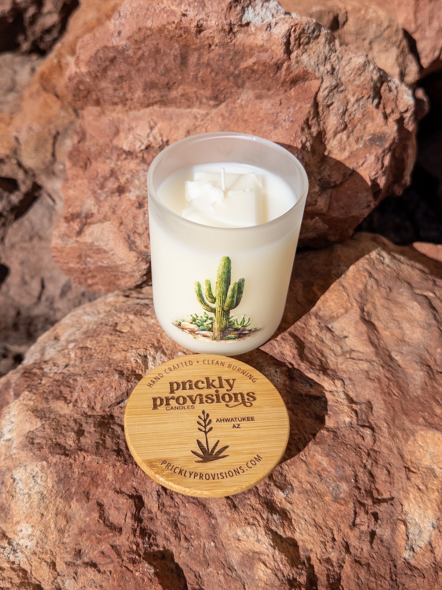 Candle with a cactus design on a rock, featuring the brand 'Prickly Provisions'.