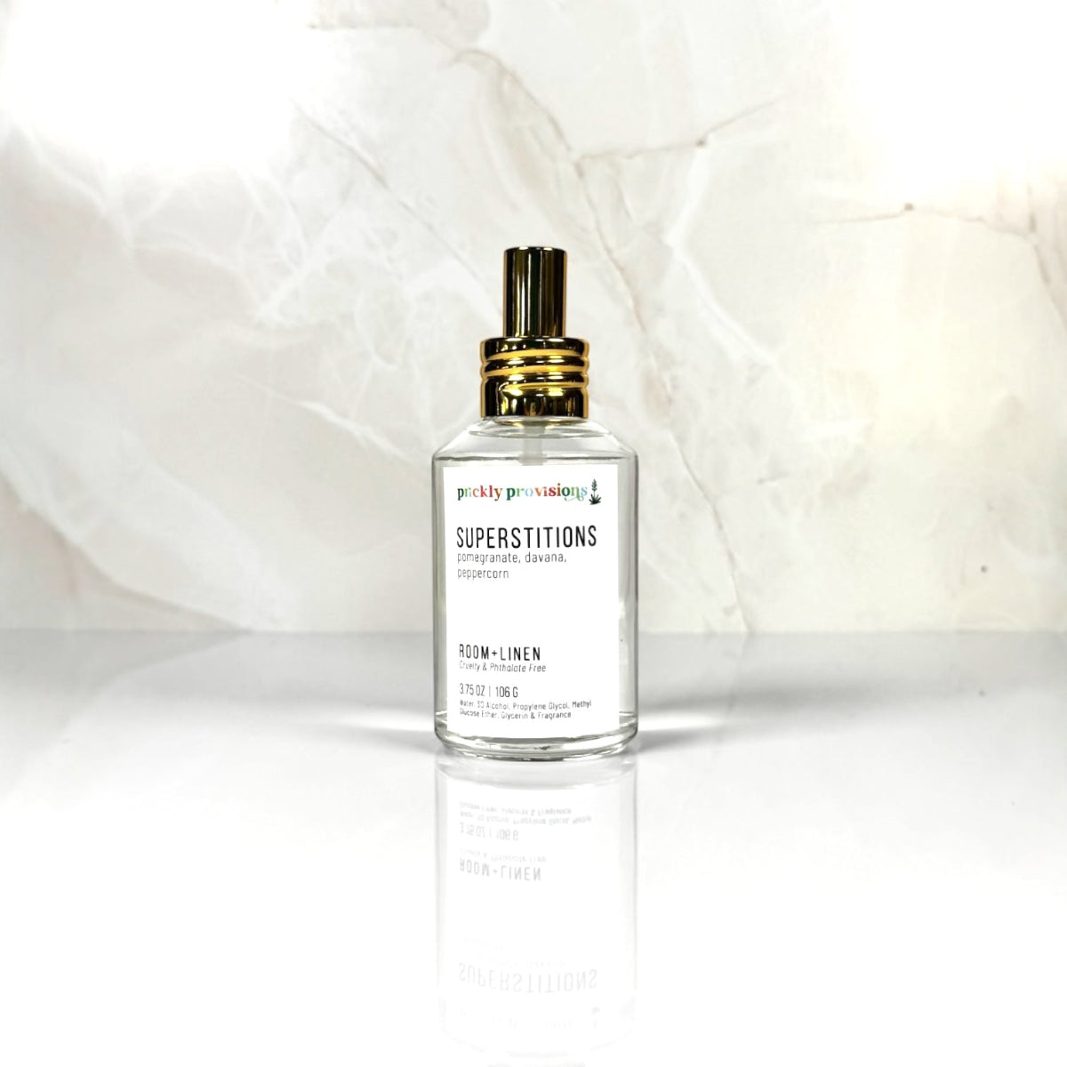 Clear spray bottle labeled 'Superstitions' on a white background. Room and linen spray with notes of Superstitions Room + Linen Spray, Pomegranate, Davana, Peppercorn.