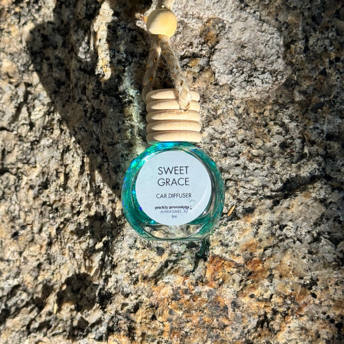Sweet Grace car diffuser hanging on a textured stone wall