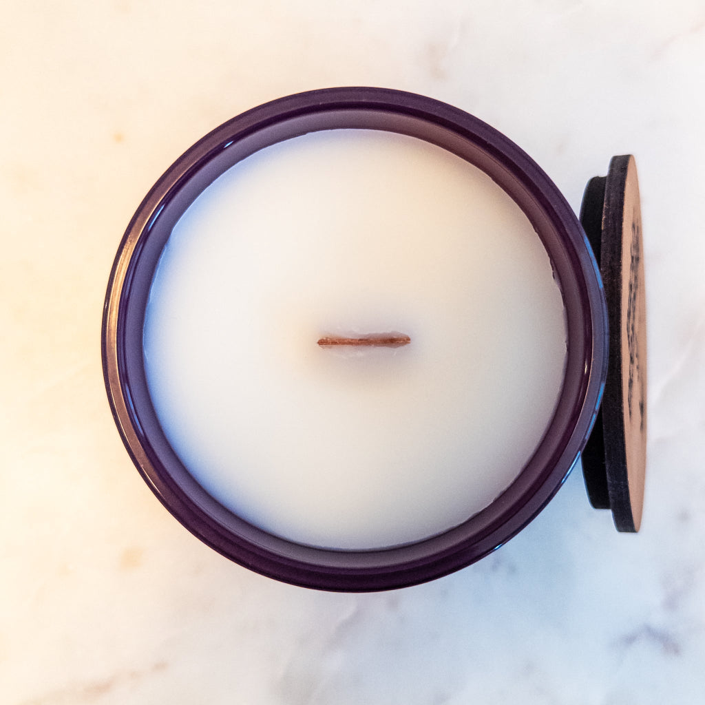 It’s Giving Hitting Zero 12 oz wood-wick candle in a matte plum glass vessel.