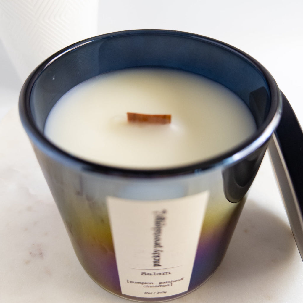 Salem 12 oz wood-wick candle in an iridescent black glass vessel with coordinating metal lid.