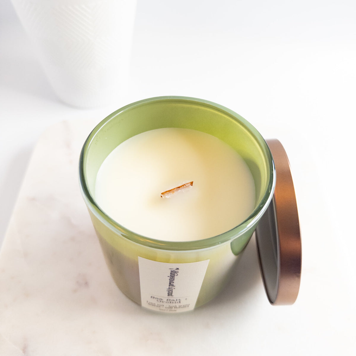 Candle in a green container with a white label on a white background