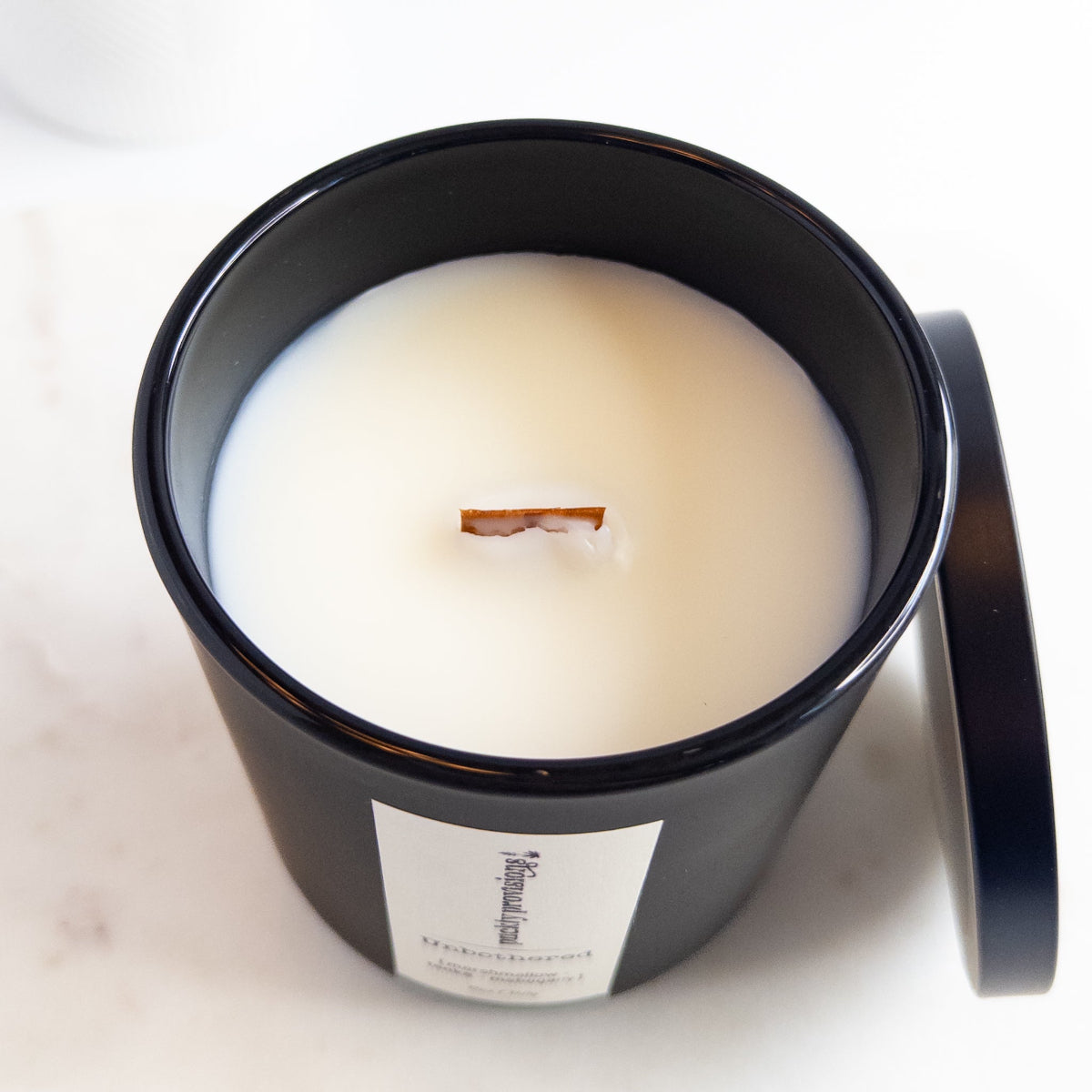 White candle in a black container with a label on a white background