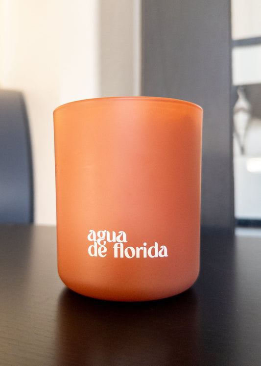 Orange candle with 'agua de floridá' text on a dark surface
