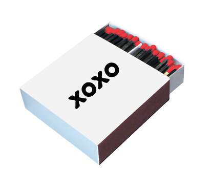Angled view of a white XOXO matchbox with black matches and bright red tips
