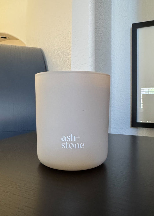 Ash candle container with 'ash + stone' branding on a dark surface.