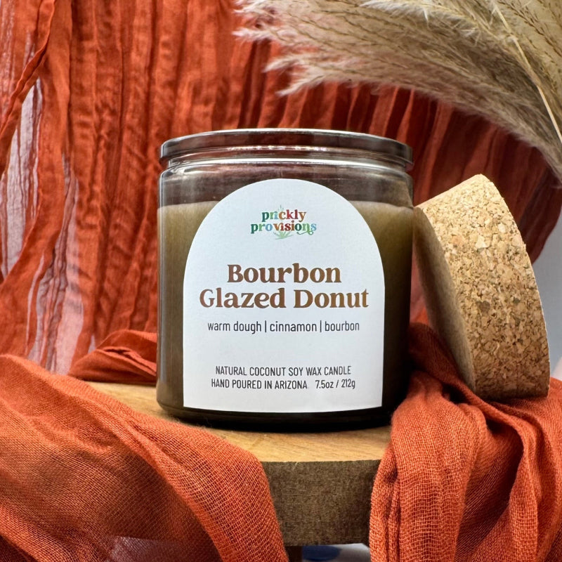 Jar of 'Bourbon Glazed Donut' candle with decorative elements on a wooden surface.