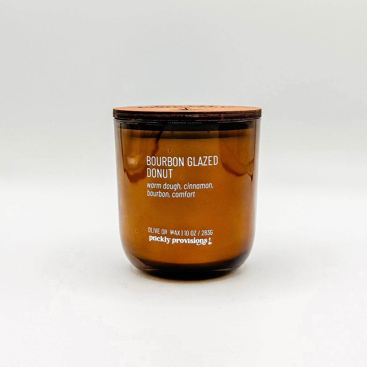 A brown glass jar candle labeled 'Bourbon Glazed Donut' with white wax, indicating a scent of warm dough, cinnamon, bourbon, and comfort.