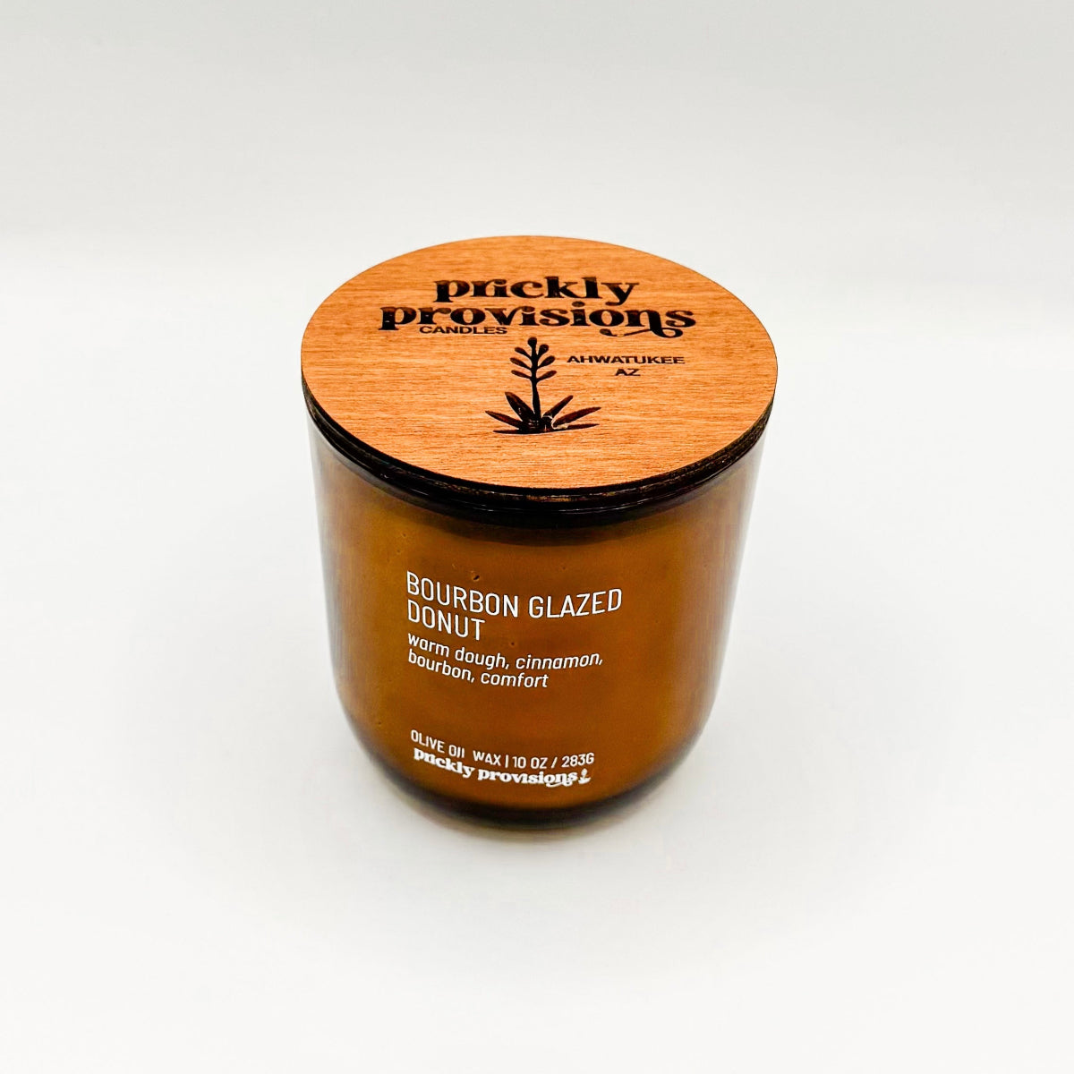 A brown glass jar candle labeled 'Bourbon Glazed Donut' with white wax, indicating a scent of warm dough, cinnamon, bourbon, and comfort.