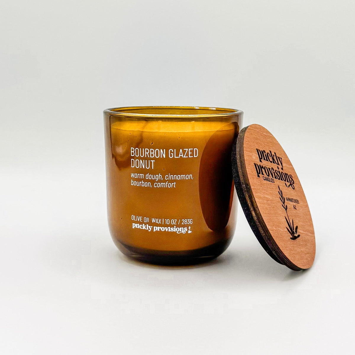 A brown glass jar candle labeled 'Bourbon Glazed Donut' with white wax, indicating a scent of warm dough, cinnamon, bourbon, and comfort.