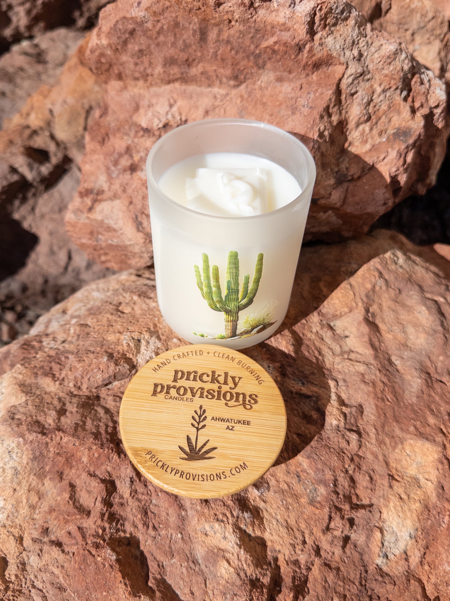 Candle with a cactus design on a rock, featuring the brand 'Prickly Provisions'.