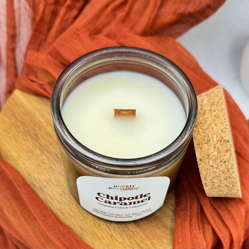Candle labeled 'Chipotle Caramel' on a wooden surface with orange fabric