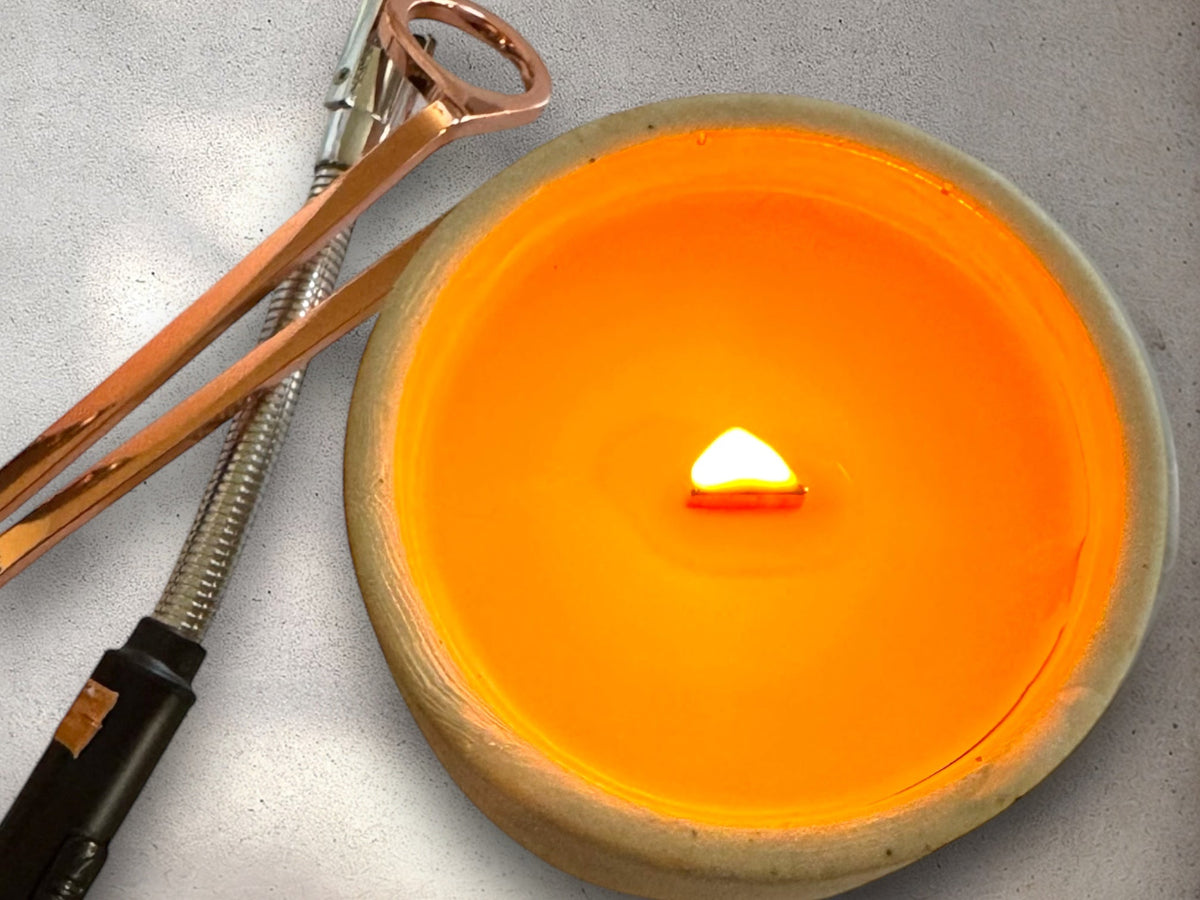 Concrete candle with a crackling wood wick on a white table with a lighter and wick trimmer