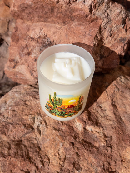 Candle in a desert-themed container on a rocky surface