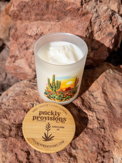 Candle with a desert design label on a rock surface, featuring 'Prickly Provisions' brand.