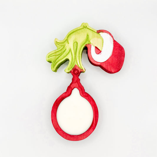 A Grinch hand holding a Christmas ornament shaped wooden dough bowl candle with 3 wicks