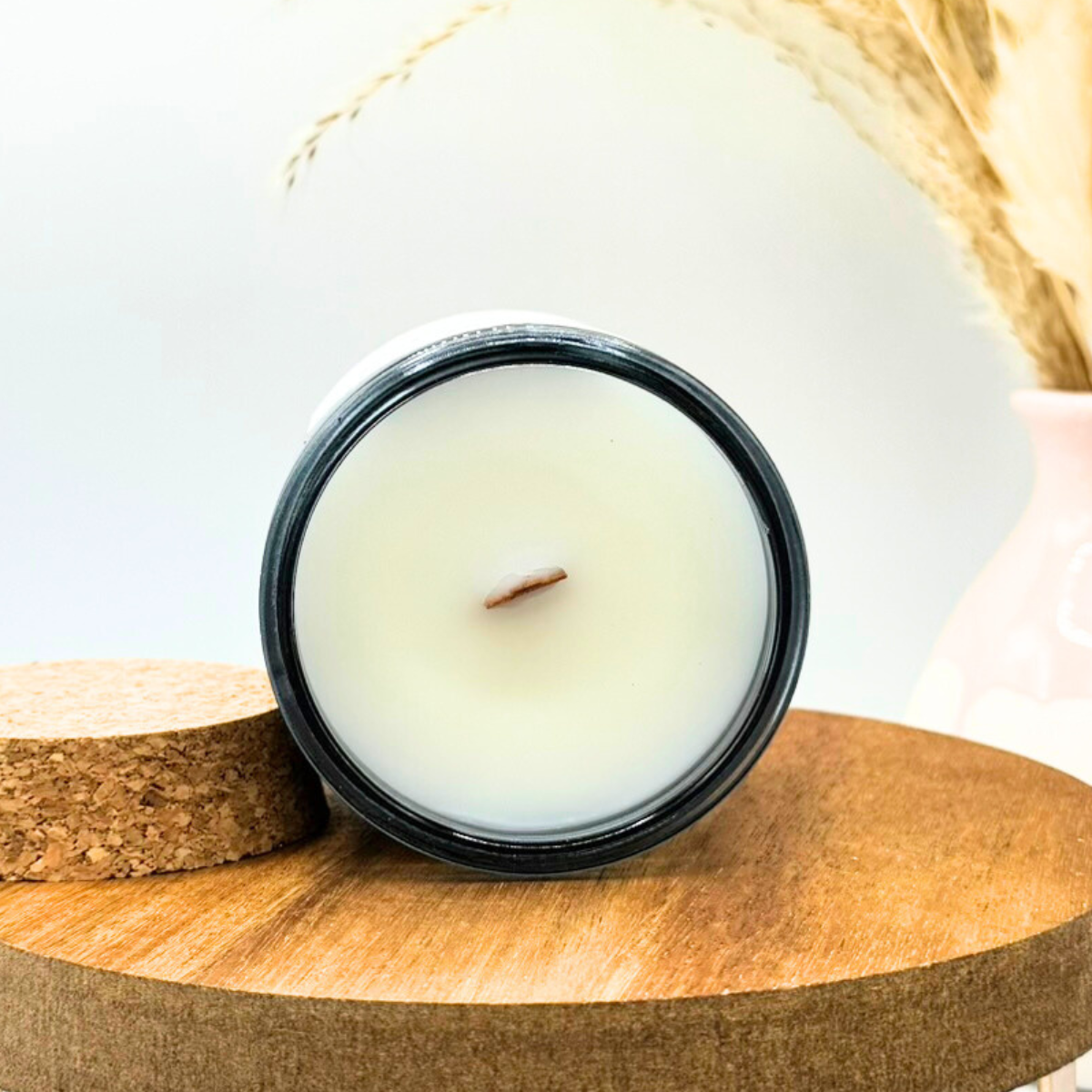 Candle in a black container on a wooden surface with a white background