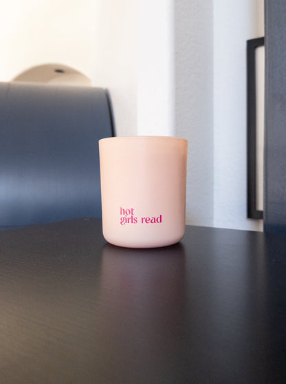 Pink candle with 'hot girls read' text on a dark surface