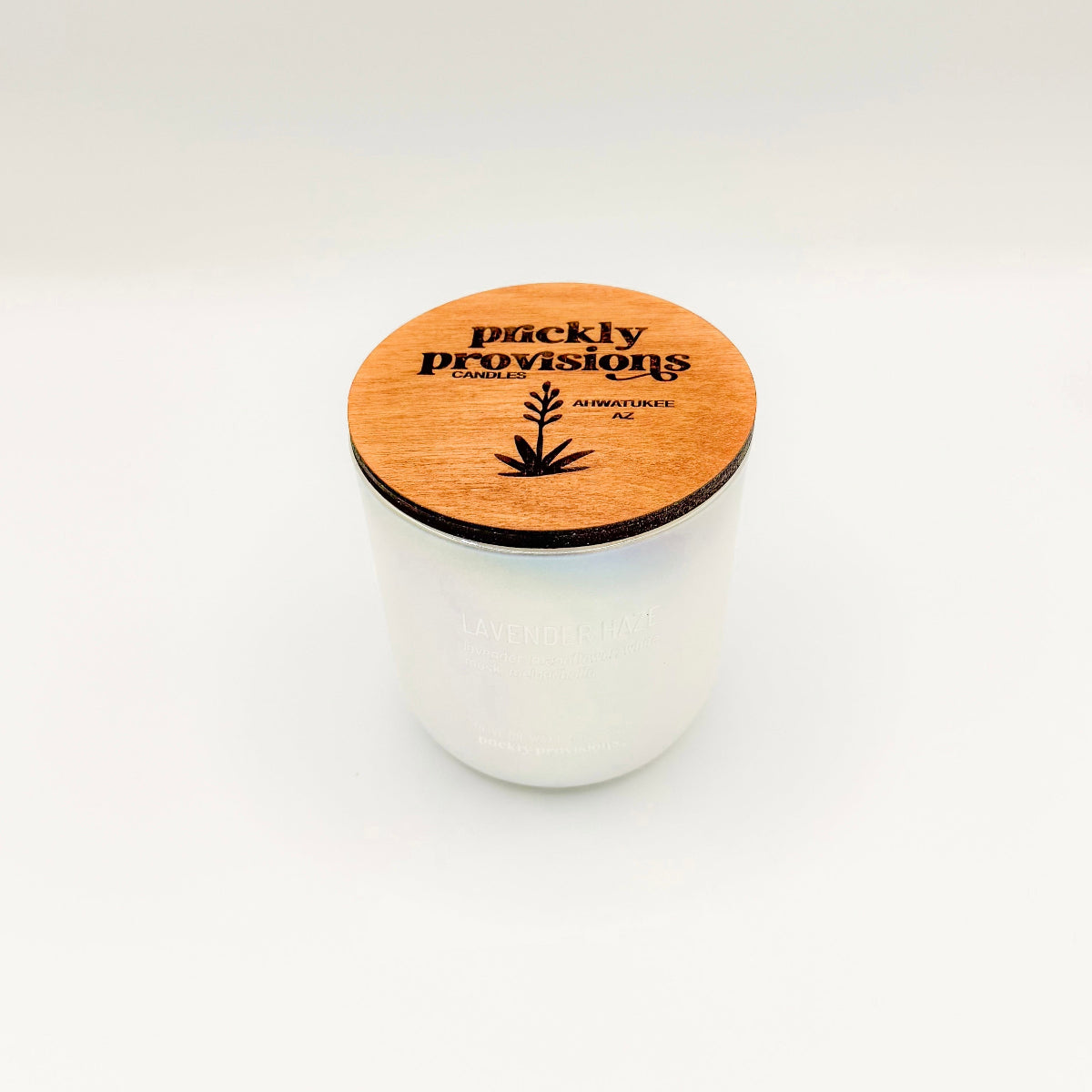 An opal white iridesent glass candle labeled 'Lavender Haze' with additional text indicating olive oil, lavender, moonflower, white musk, melancholia. The candle is in a glass jar with a wooden lid.