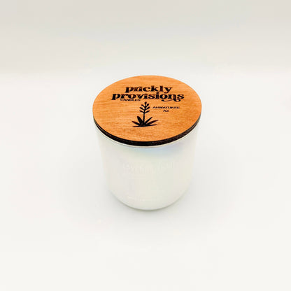 An opal white iridesent glass candle labeled 'Lavender Haze' with additional text indicating olive oil, lavender, moonflower, white musk, melancholia. The candle is in a glass jar with a wooden lid.