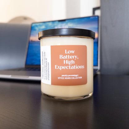 Low Battery, High Expectations 10 oz double-wick office candle with terracotta label and black metal lid.
