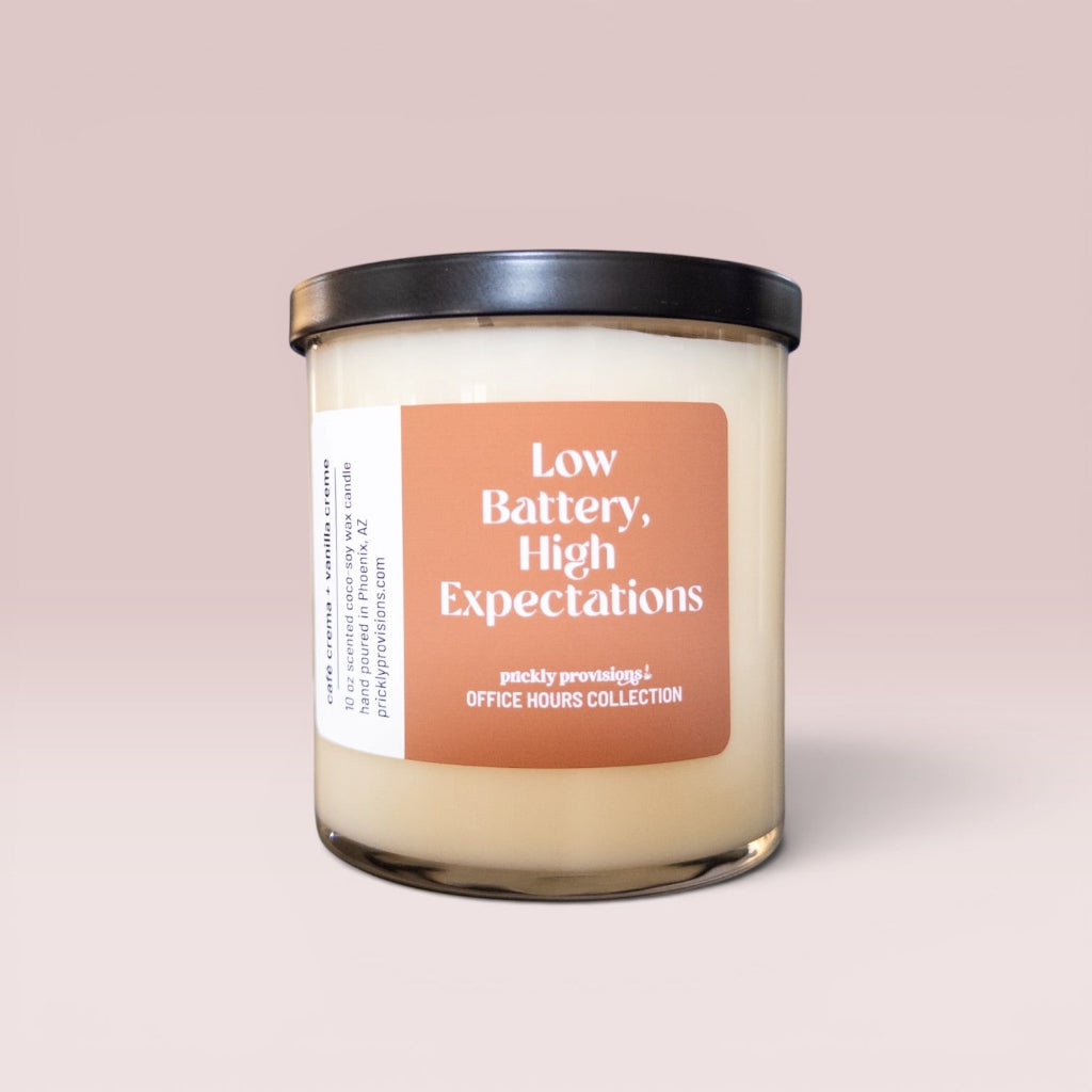 Low Battery, High Expectations 10 oz double-wick office candle with terracotta label and black metal lid.