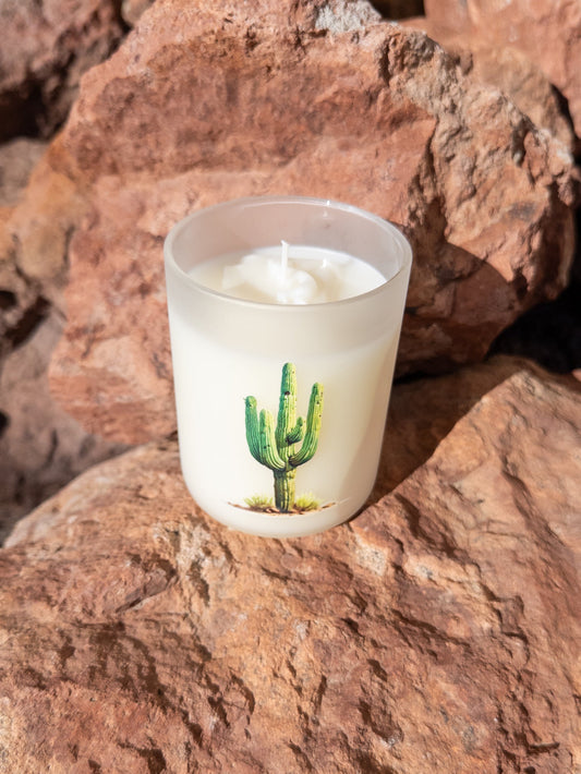 Candle in a glass container with a cactus design on a rocky surface