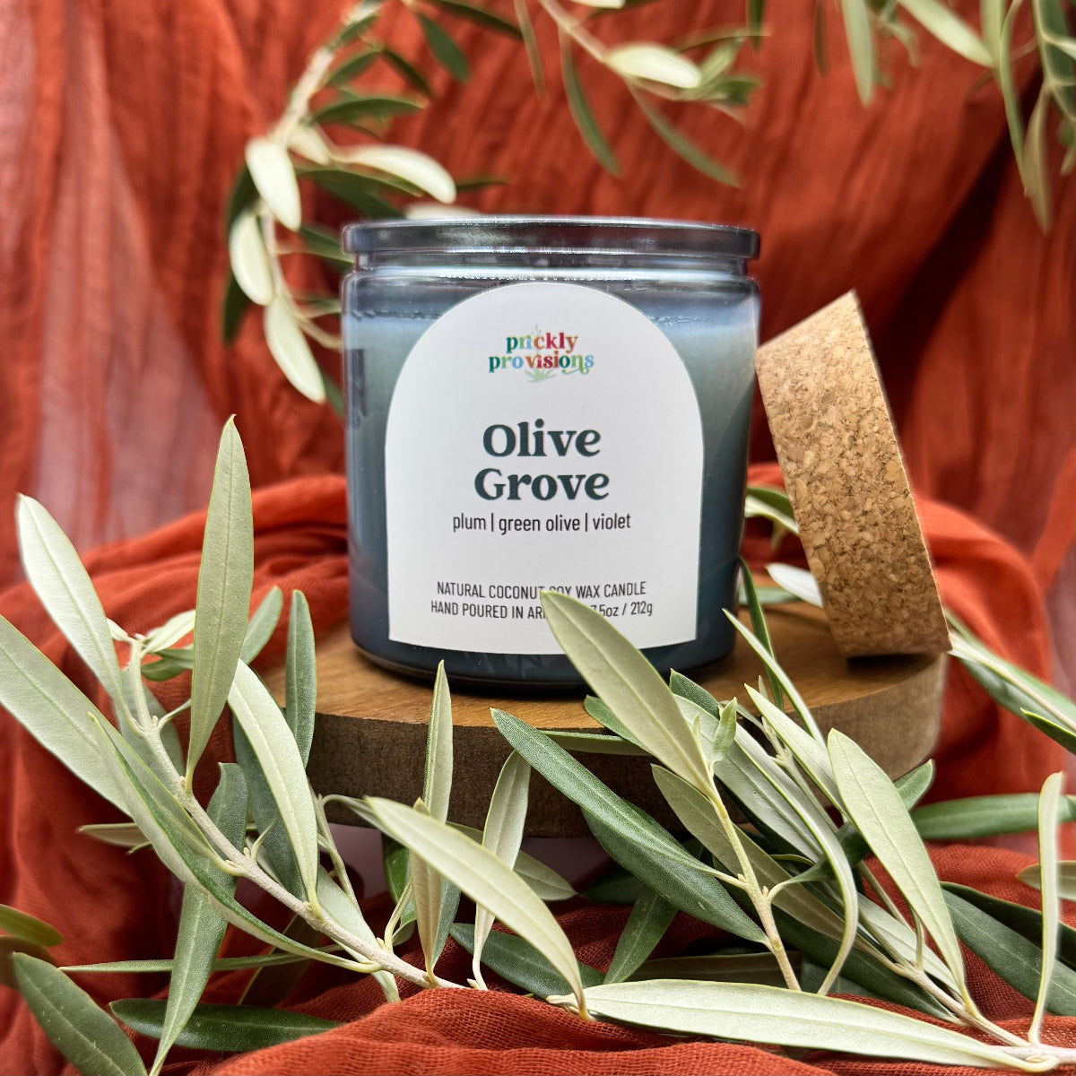 Candle labeled 'Olive Grove' with olive leaves on a wooden surface