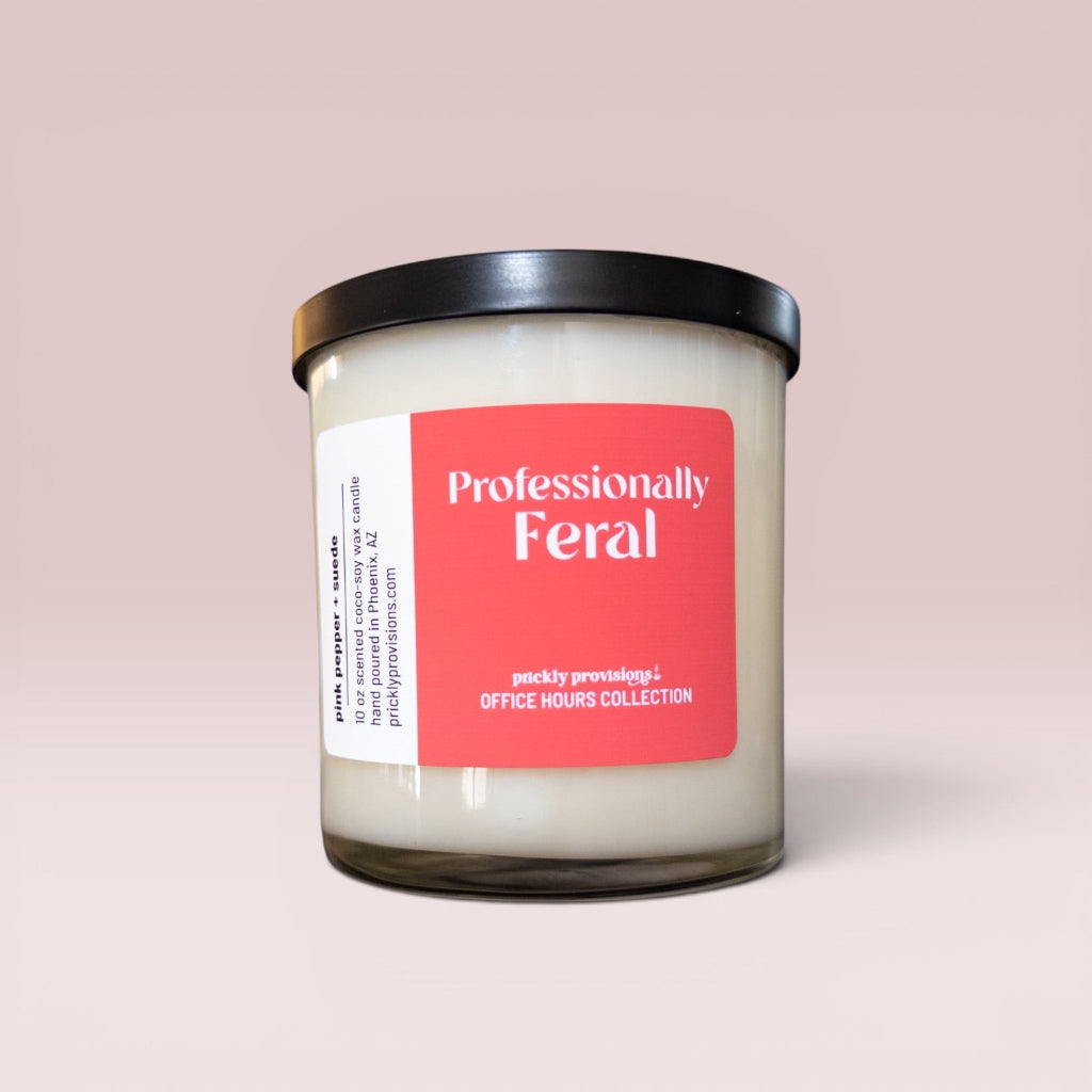 Professionally Feral 10 oz double-wick office candle with a coral-red label and black metal lid.