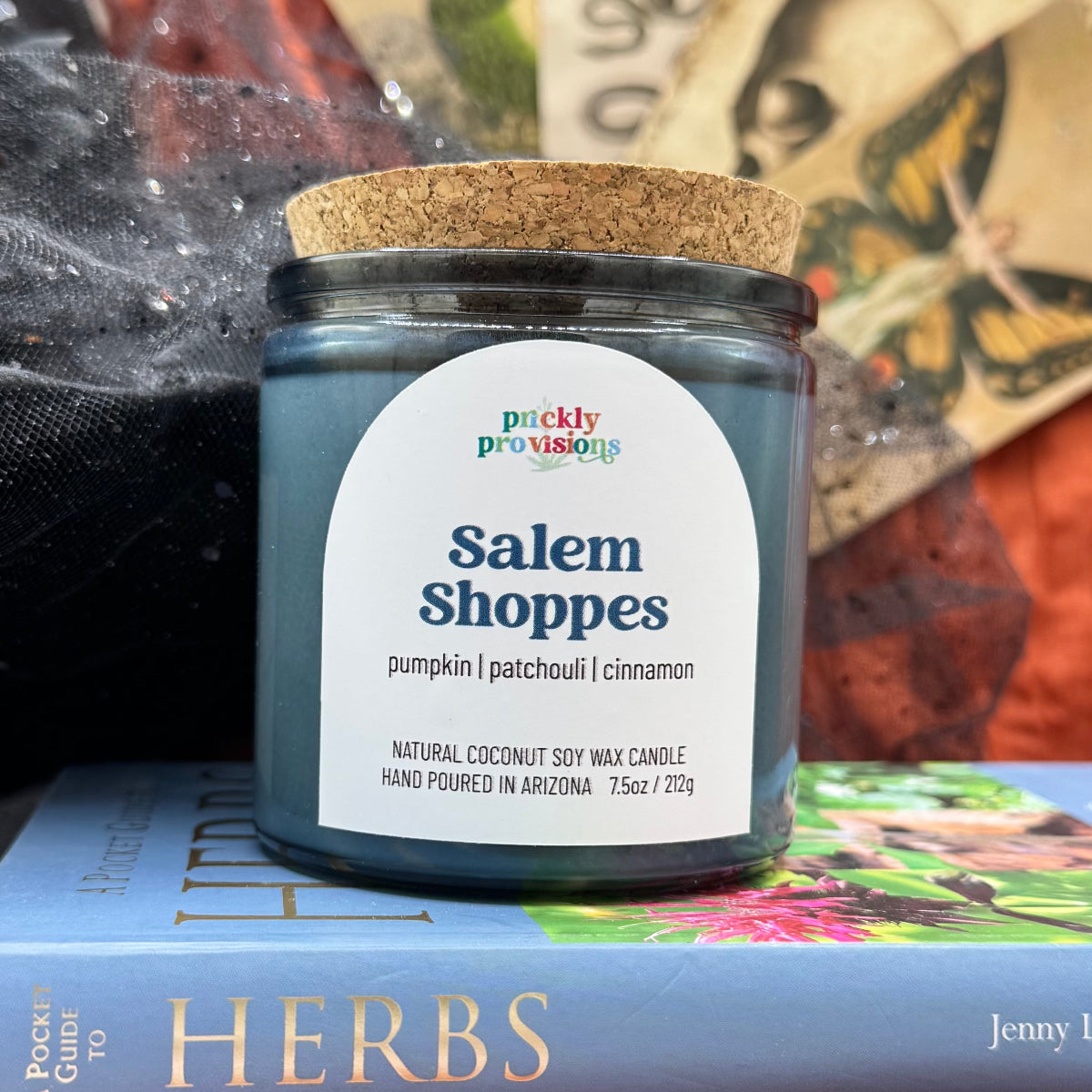Candle jar labeled 'Salem Shoppes' by Prickly Provisions on a book with a colorful background.