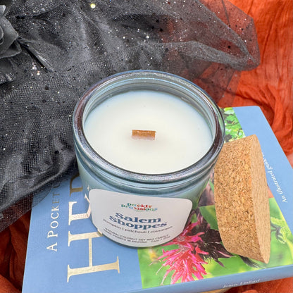 Candle in a blue jar labeled 'Salem Sippies' on top of a book with decorative elements.