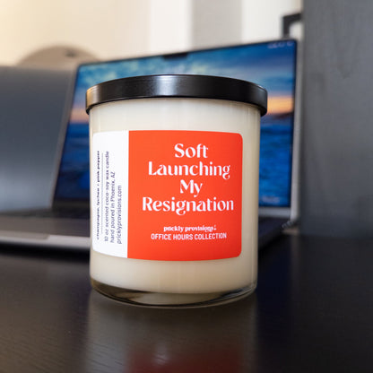 Soft Launching My Resignation 10 oz double-wick office candle with an orange-red label and black metal lid.