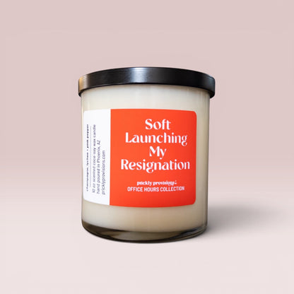Soft Launching My Resignation 10 oz double-wick office candle with an orange-red label and black metal lid.