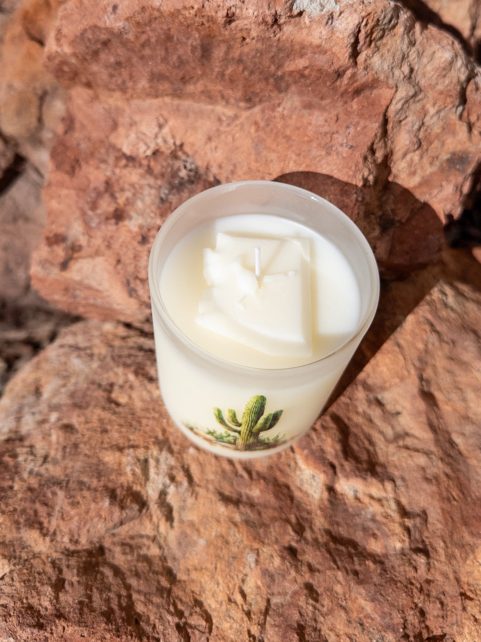A candle with a cactus illustration on a stone surface