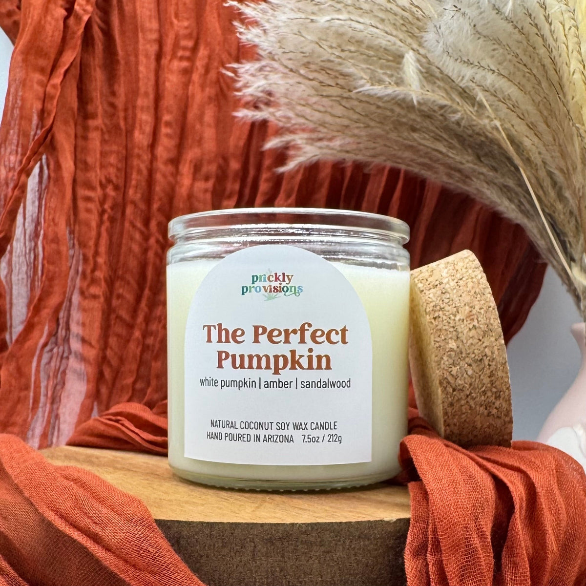 Candle labeled 'The Perfect Pumpkin' by Prickly Provisions on a wooden surface with autumn-themed decor.