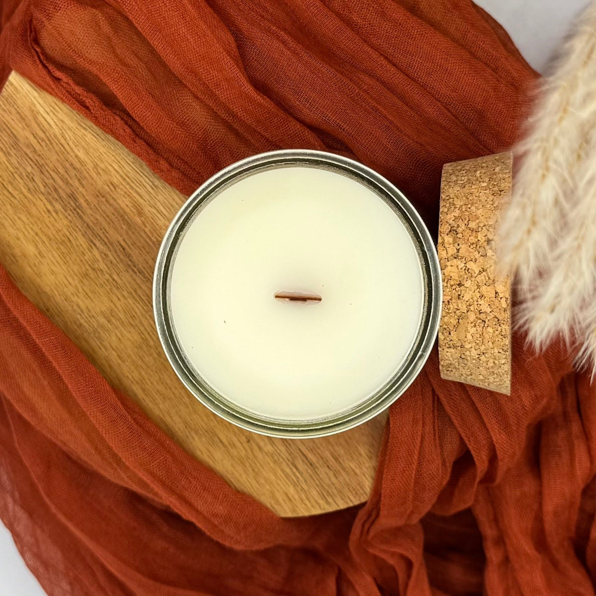 Candle in a metal container on a wooden surface with orange fabric
