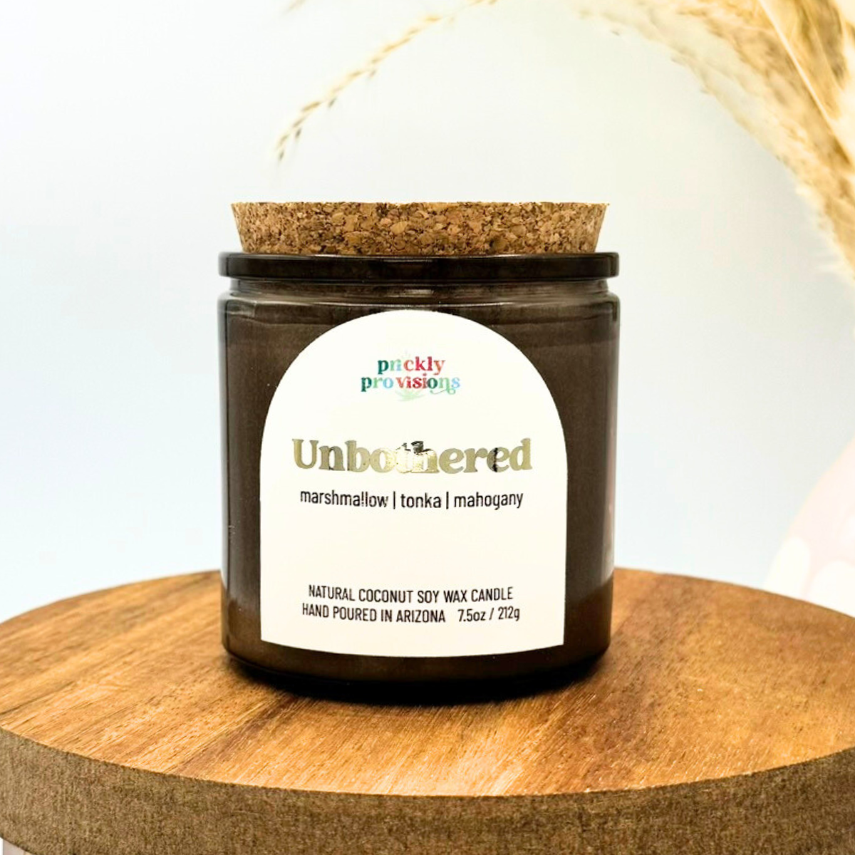 Candle jar with cork lid on a wooden surface, featuring a label with product details.