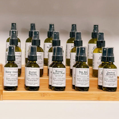 Sea Salt + Orchid room and linen spray bottles displayed on a wooden shelf
