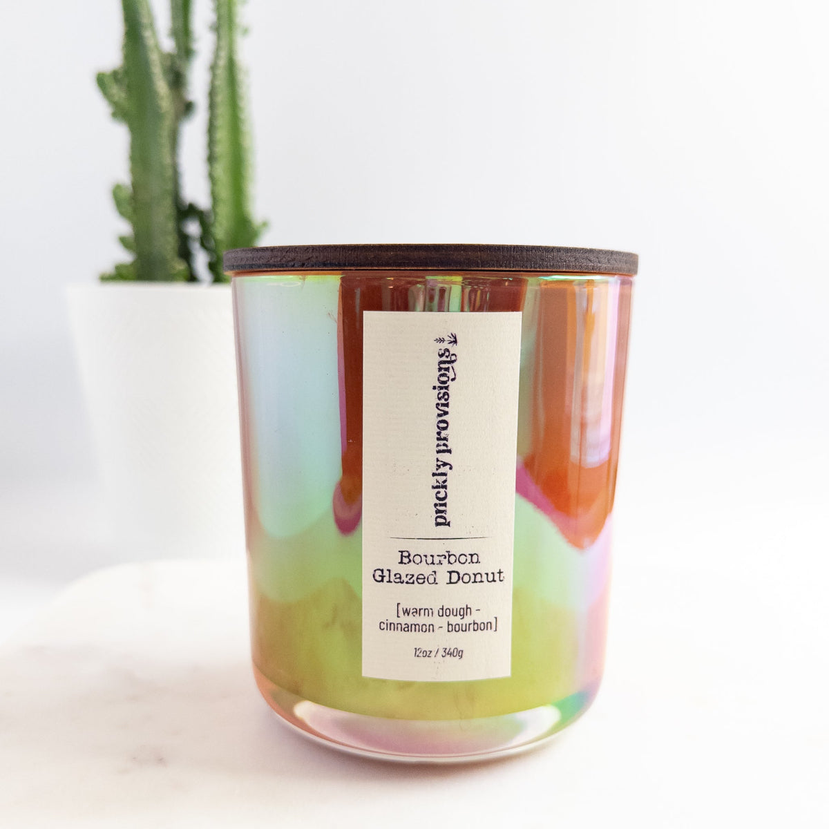 Candle with a label on a white surface, featuring a plant in the background.
