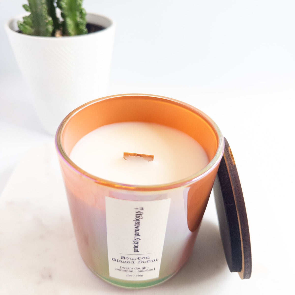 Candle with a wooden lid on a white surface next to a cactus plant.