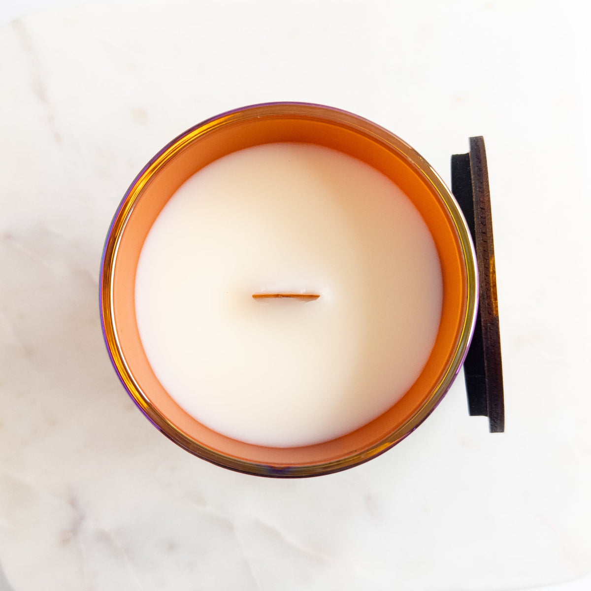 White candle in an amber glass jar with a wooden lid on a white background