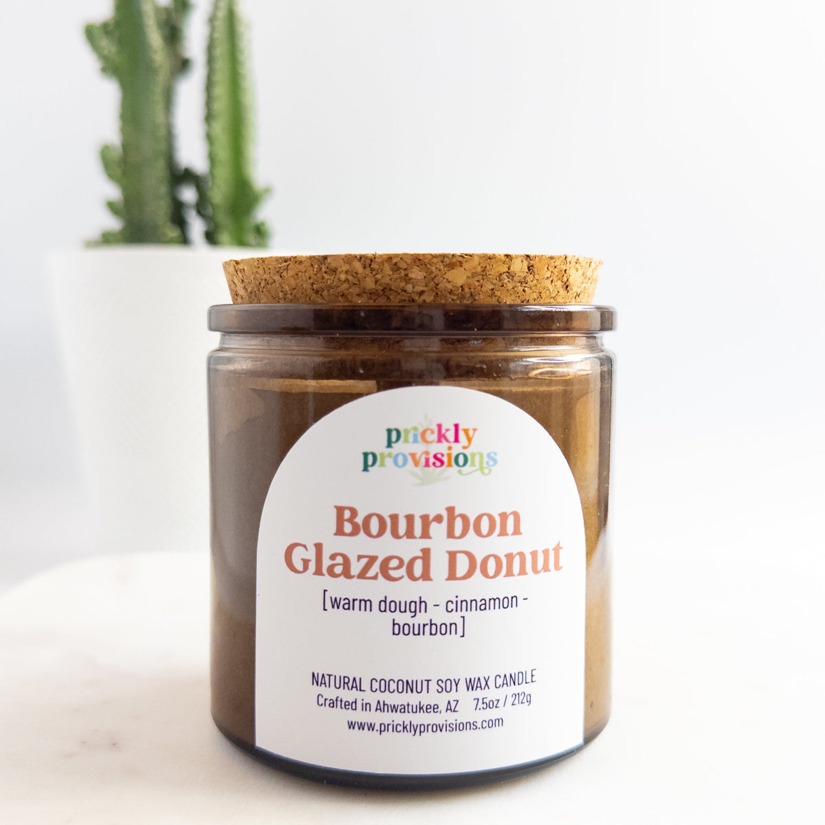 Jar of 'Bourbon Glazed Donut' candle by Prickly Provisions with a cork lid on a white surface.