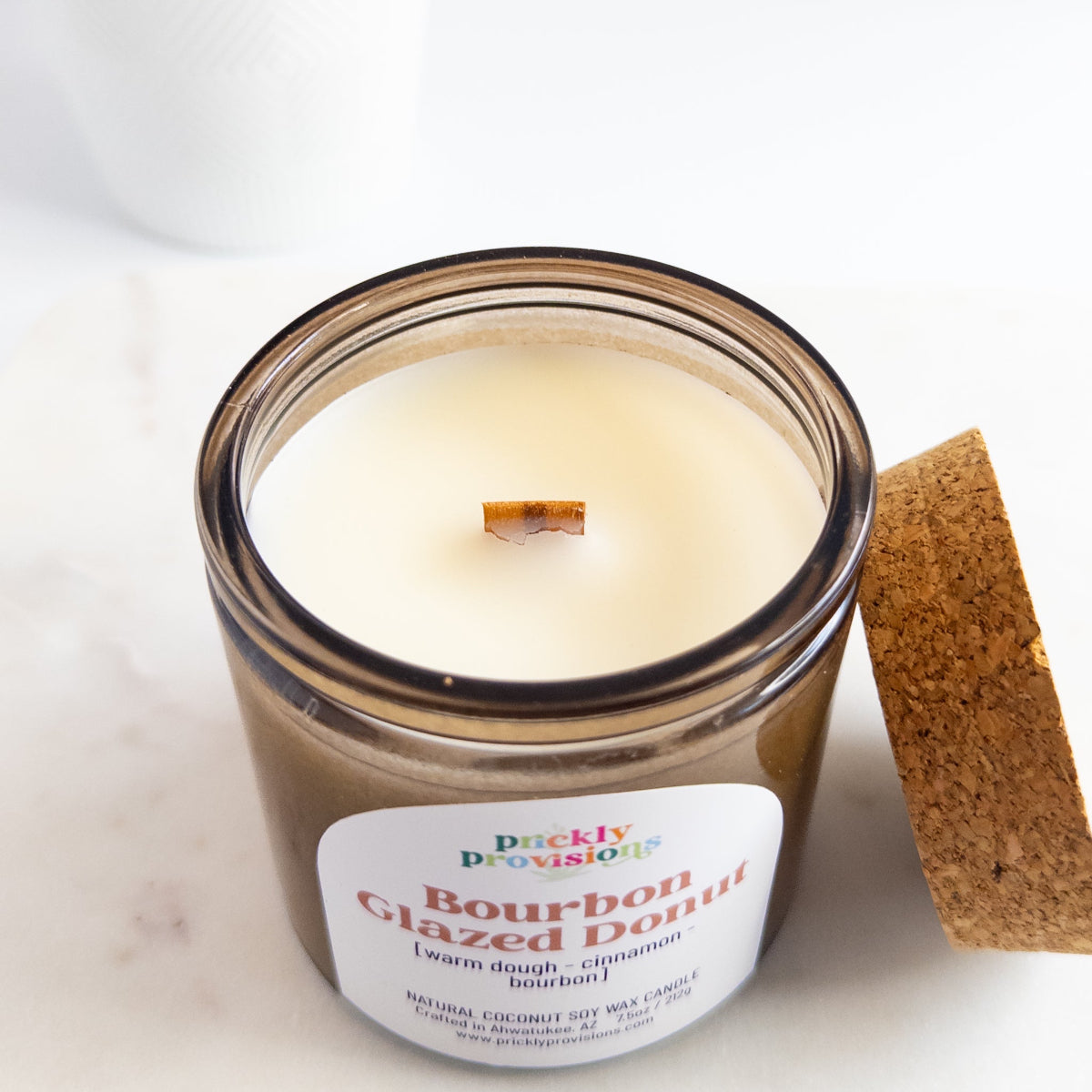 Candle in a glass jar with a wooden coaster on a white surface