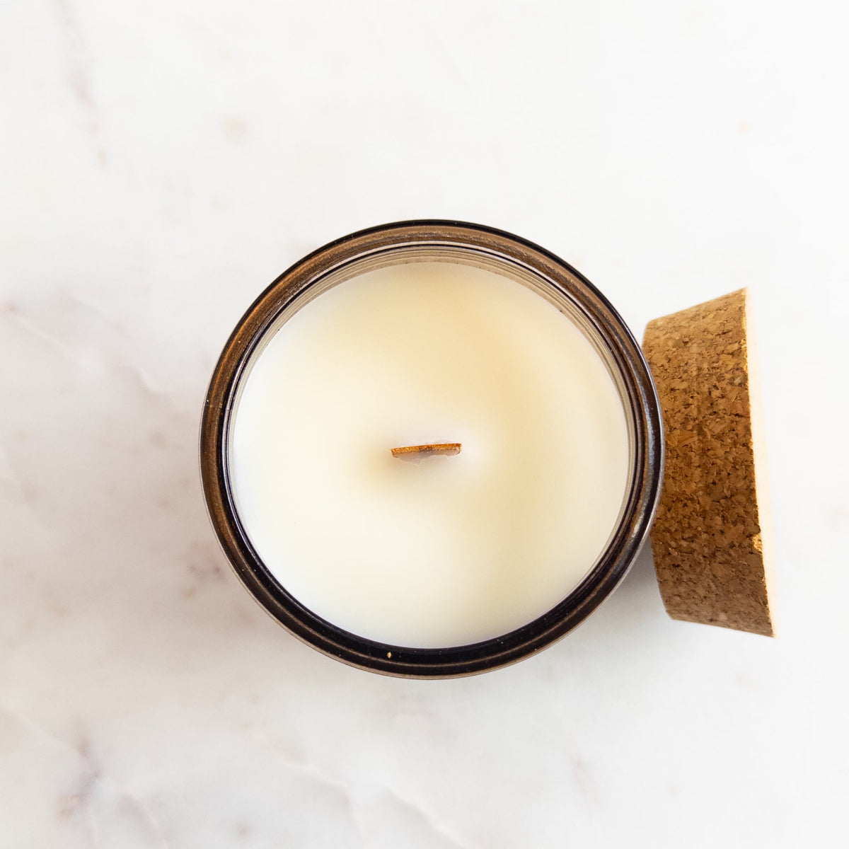 Candle in a glass jar with a wooden lid on a white marble surface