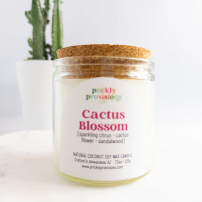 Candle jar labeled 'Cactus Blossom' by Prickly Provisions with a cactus plant in the background.
